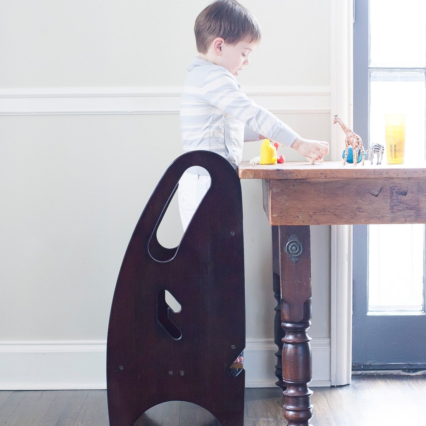 A boy stands at a table on the 3-in-1 Growing Step Stool.