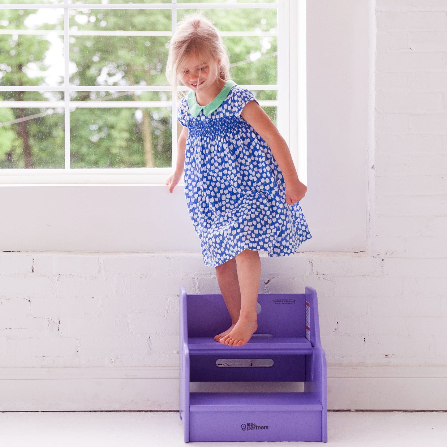 A young girl is standing on the StepUp Step Stool in Lilac.