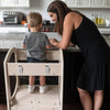 A young boy is standing in the Chef Series Learning Tower.  His Mom is there too.