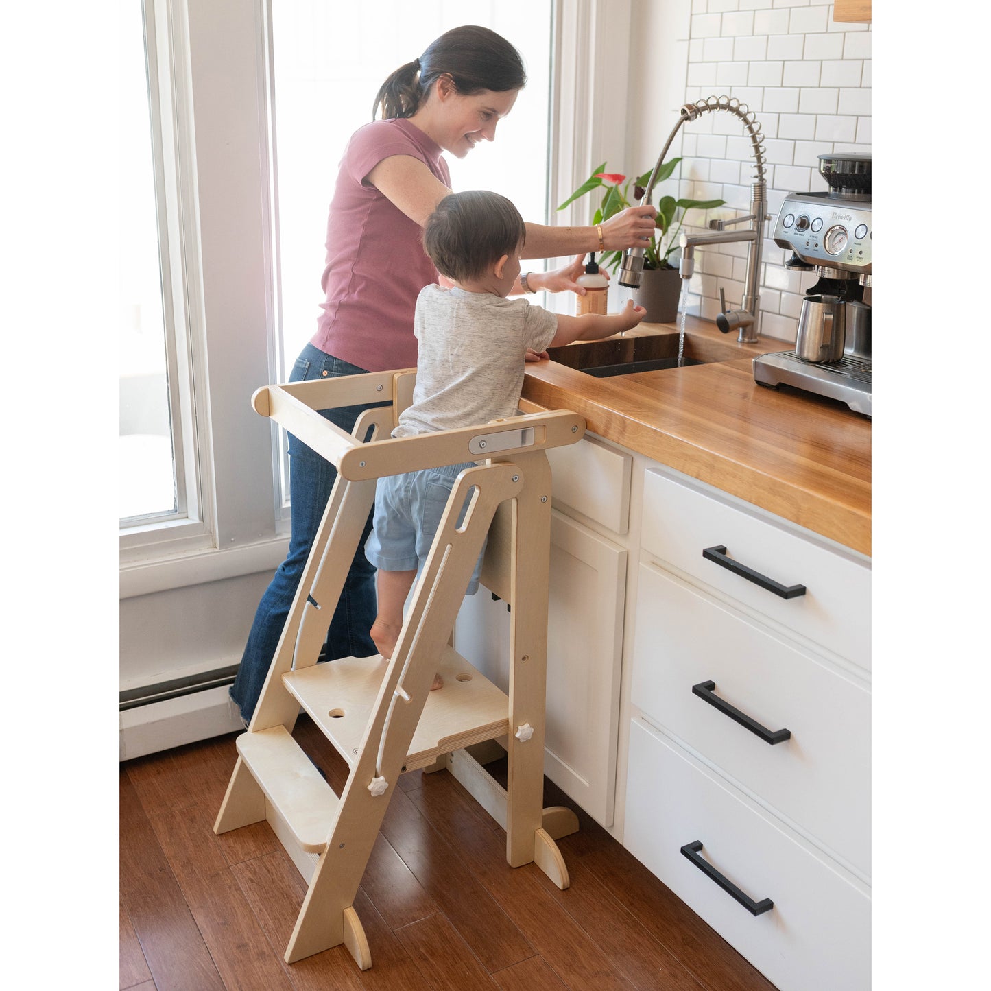 A boy stands at the kitchen sink in the Learn 'N Fold Learning Tower in Natural color.