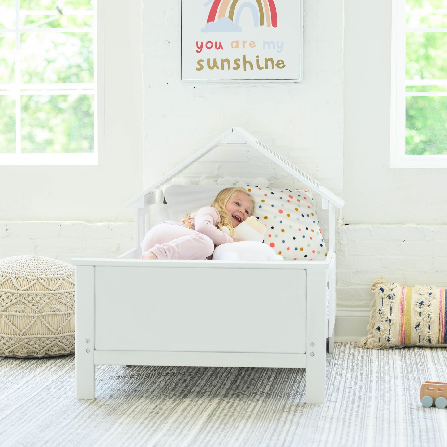 A young girl is laying in the Lil House Toddler Bed.