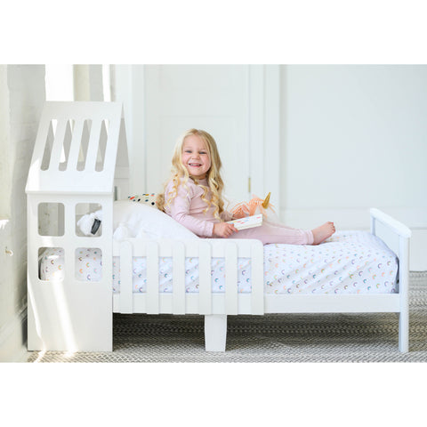 A young girl is sitting in the Lil House Toddler Bed.