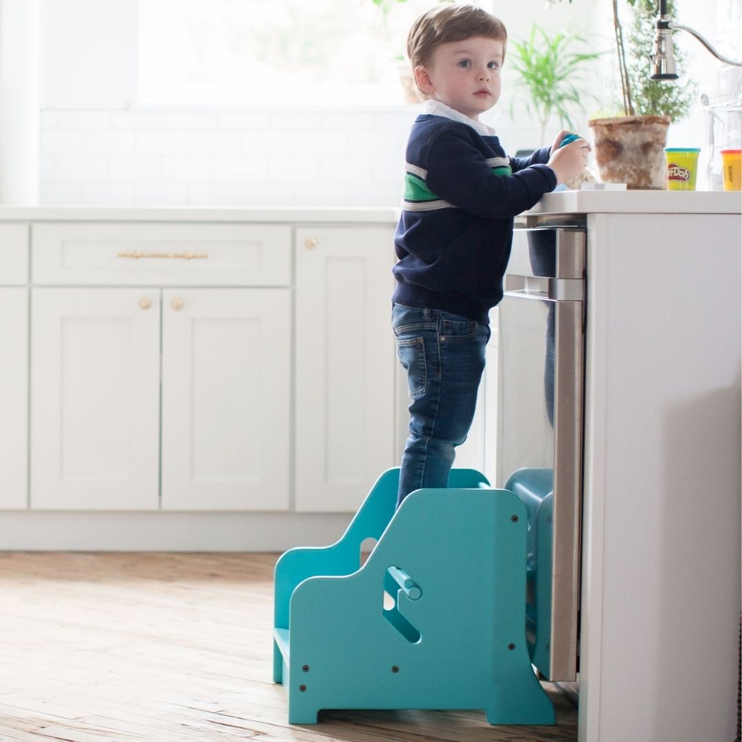 A boys stands on the StepUp Step Stool at the kitchen counter.