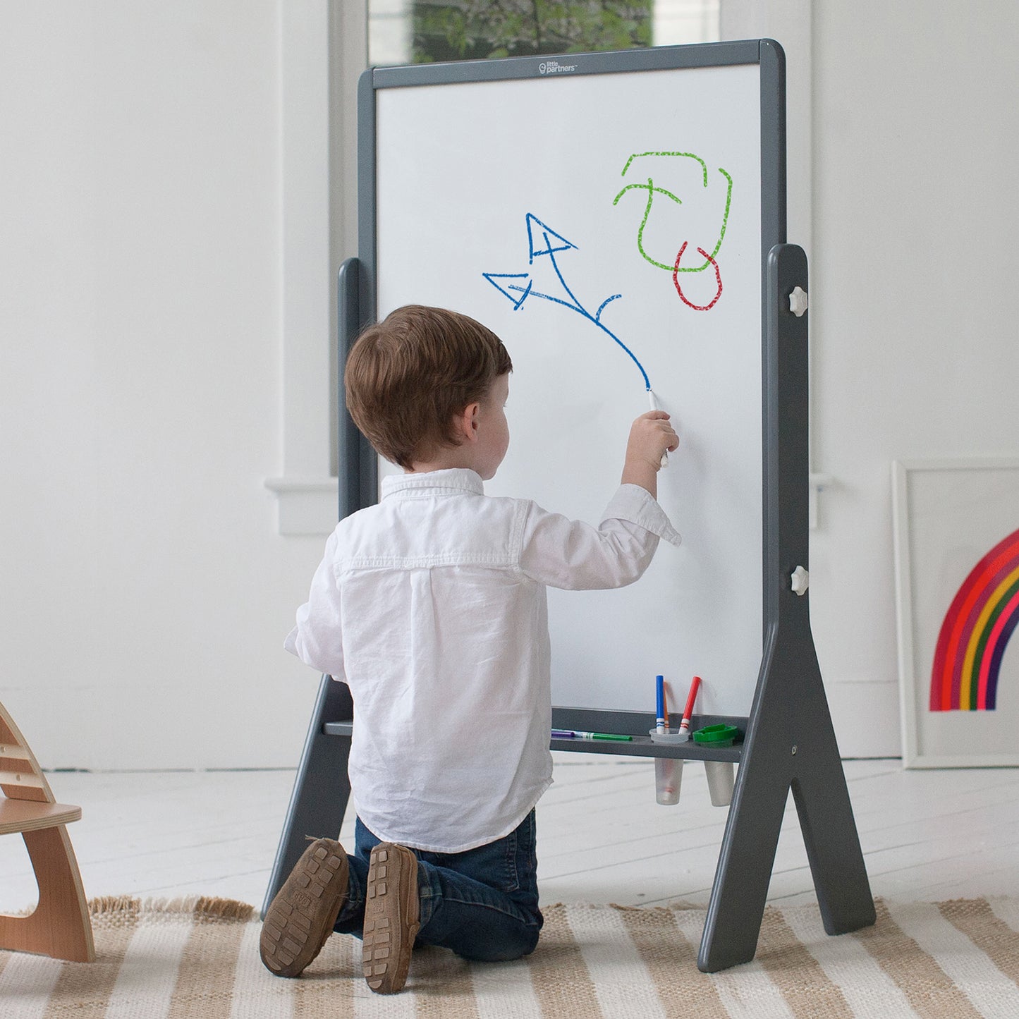 A boy is kneeling in front of the Contempo Art Easel.  He is coloring with markers.