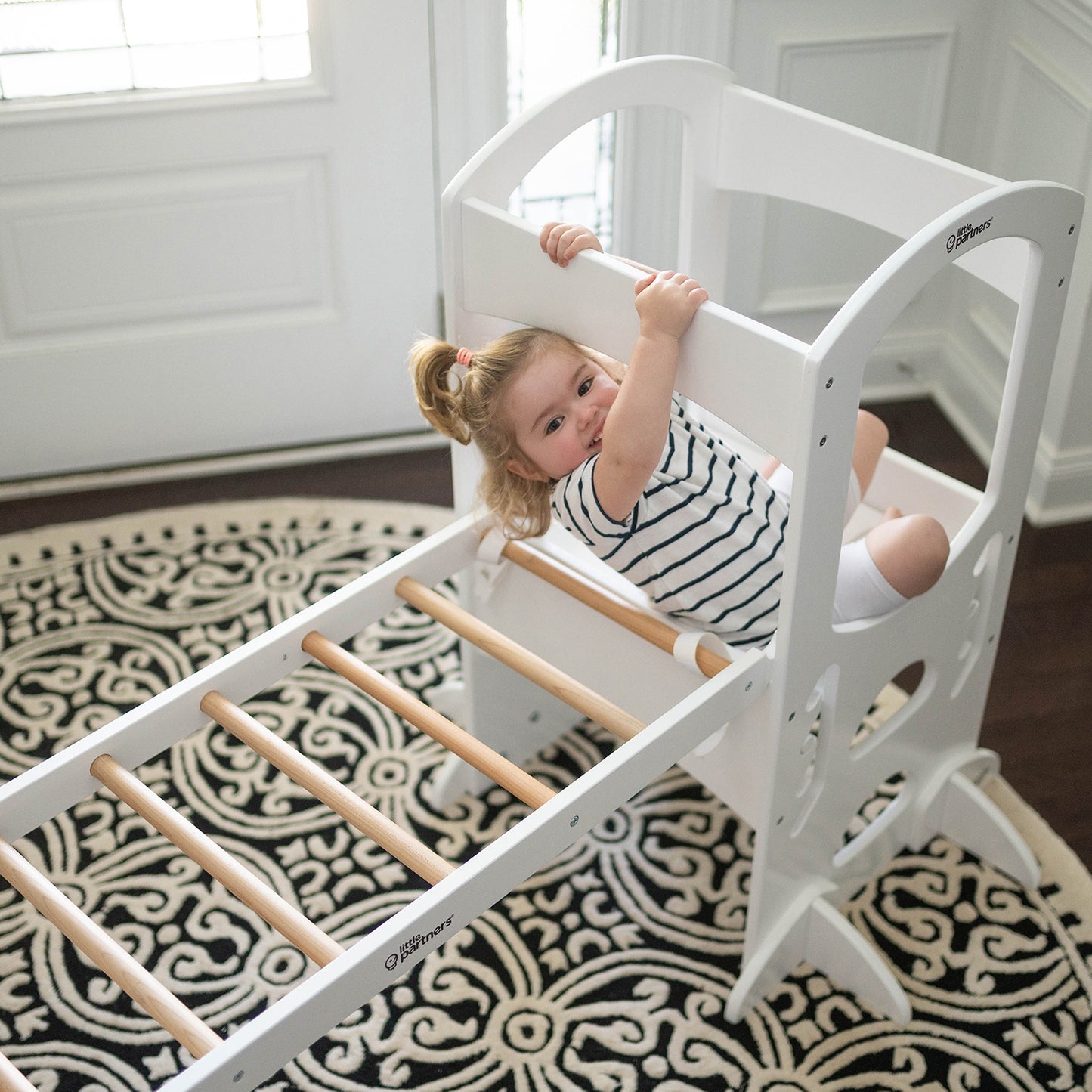 A young girl is climbing on the climbing ladder while it is securely attached to the Learning Tower.