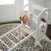 A young girl is climbing on the climbing ladder while it is securely attached to the Learning Tower.