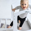 A young child is standing in the Learning Tower, which is connected to the Climbing Ladder.